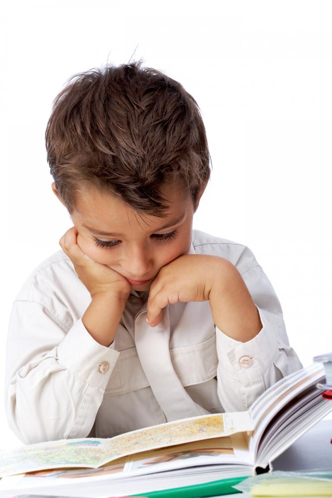 A young boy resting his chin on his hands while looking down thoughtfully at an open textbook on a white background.